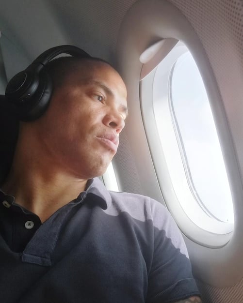 A close-up of a person wearing noise-canceling headphones on a busy airplane. The person is looking at a laptop with a focused expression, seemingly undisturbed by the surrounding chaos. The headphones are a key element, symbolizing their ability to create a quiet working environment despite the noisy setting.
