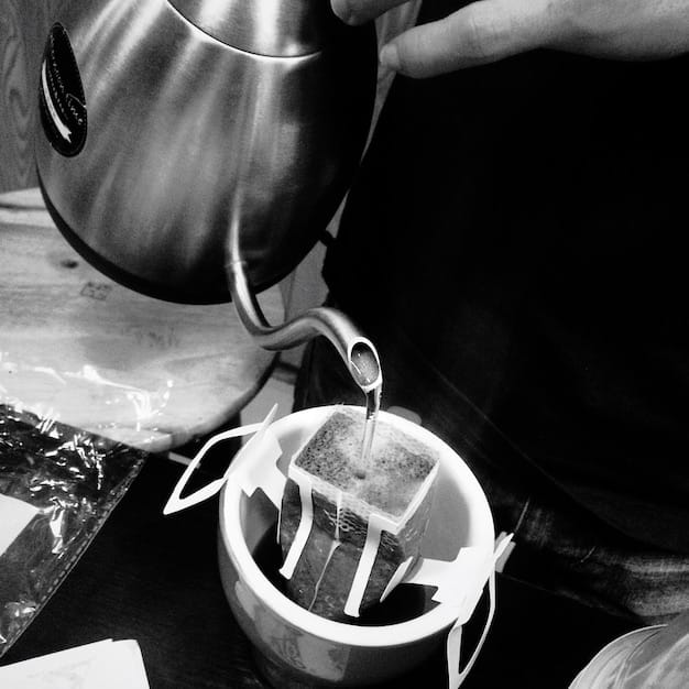 A close-up shot of a person using a pour-over coffee maker, carefully pouring hot water over freshly ground coffee. The image highlights the manual and artisanal aspect of this brewing method.