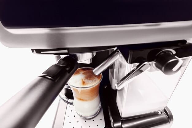 A sleek, modern espresso machine with a built-in grinder and milk frother. The machine is shown in operation, dispensing a perfect shot of espresso into a glass cup.