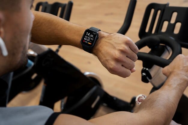 Close-up of the smartwatch screen displaying a live heart rate reading during an intense workout session. The background is blurred, showing gym equipment such as dumbbells and a treadmill.
