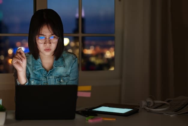 A person wearing blue light glasses while working on a computer late at night, with emphasis on the glasses filtering the blue light from the screen.