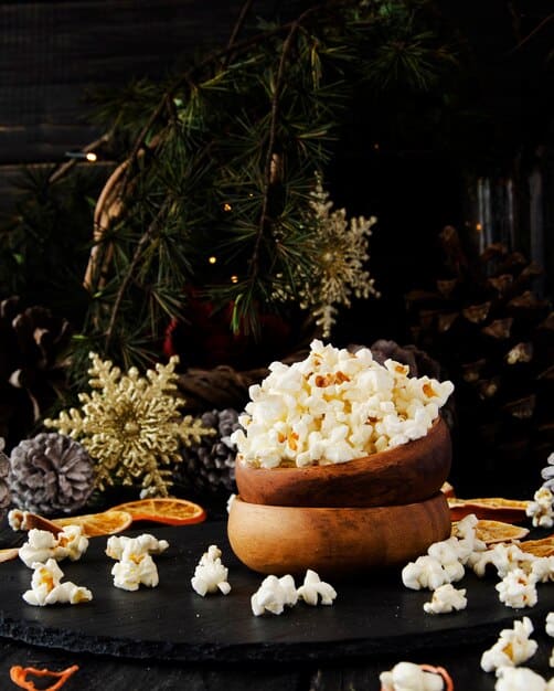 A close-up shot of a beautifully arranged gourmet popcorn gift basket with different flavors, presented on a rustic wooden surface with festive holiday decorations in the background.