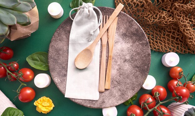 A set of bamboo cutlery (fork, knife, spoon) wrapped in a reusable cloth napkin, placed on a wooden table. The background is blurred, highlighting the natural and eco-friendly aspect of the bamboo utensils.