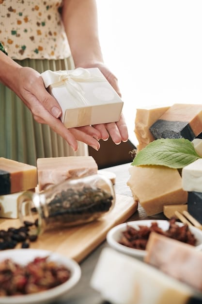 A close-up shot of a person selecting small, artisanal items for a DIY gift basket from a local market, showcasing handmade soaps, small jars of gourmet jam, and unique trinkets.