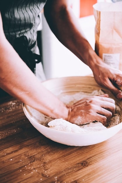 A close-up shot of a chef instructing a student how to properly knead dough during a bread-making class. The focus is on the hands and the texture of the dough, emphasizing the tactile learning experience.