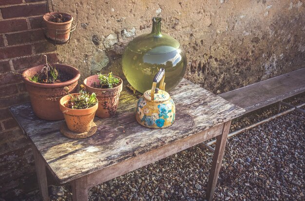 A stylish, weatherproof outdoor potting bench set up on a patio, featuring a variety of terracotta pots, gardening tools neatly arranged in containers, and a small herb garden in the background. The bench is made of reclaimed wood and has ample workspace for potting and transplanting plants.