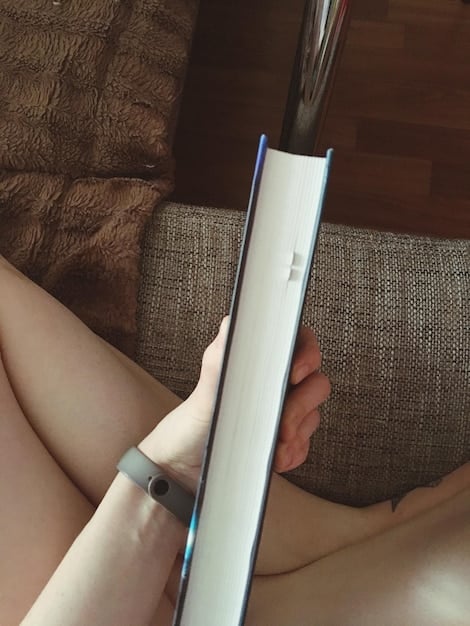 A close-up of hands holding a modern, sleek e-reader with an open book on the screen, surrounded by a comfortable, minimalist setting, implying relaxation and learning.